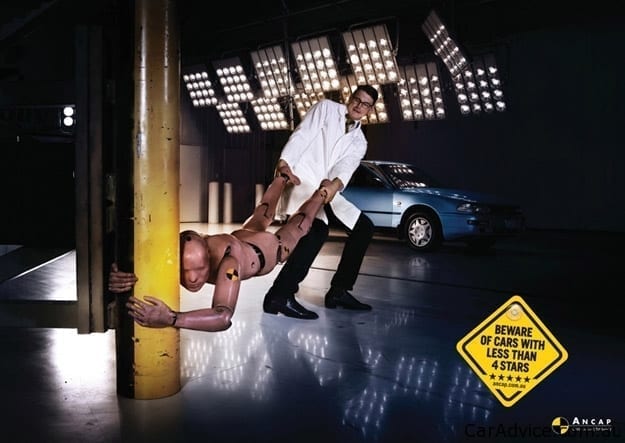 A crash-test dummy holds onto a pole as a researcher tries to drag it into a car for testing.