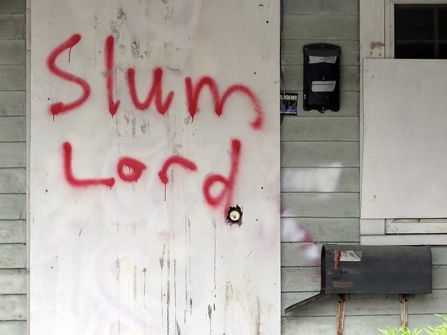 The words "Slum Lord" are scrawled in red paint on the front door of a dwelling.