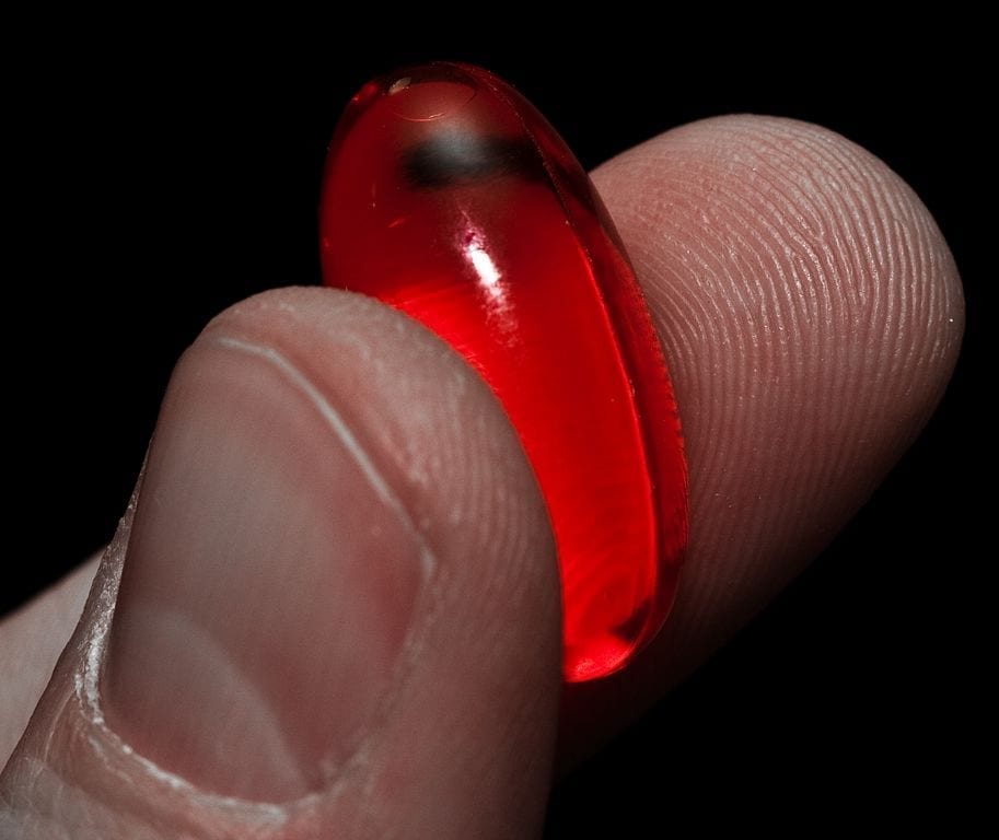 A red pill grasped between the thumb and index finger.