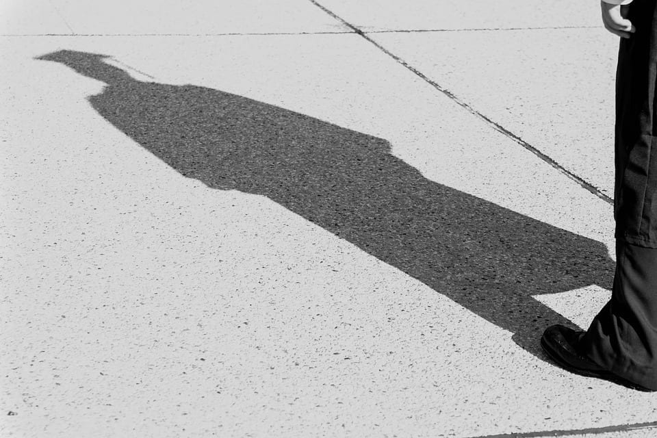 The shadow of a graduate in cap and gown falls upon the grey sidewalk.