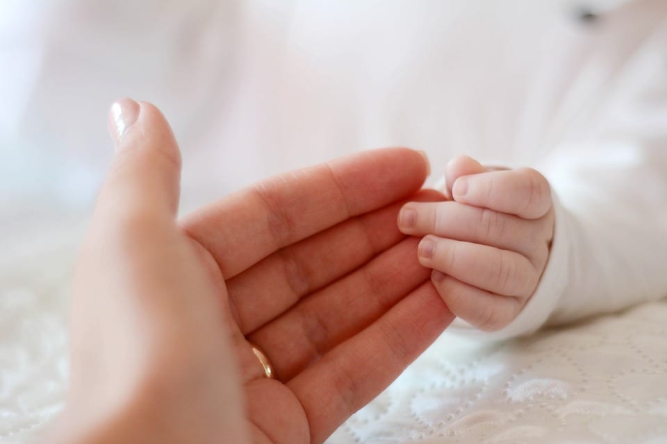 A small baby's hand clings to Mother's fingers.