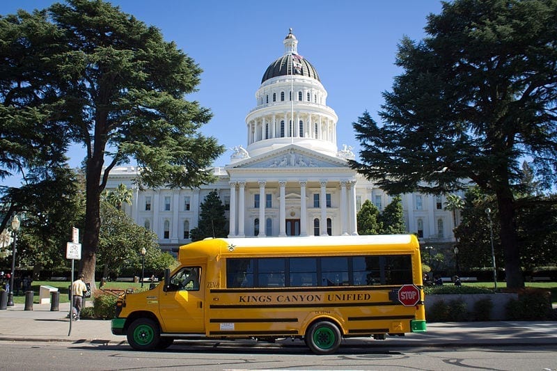 An electric school bus sits parked in front of California's capitol building.