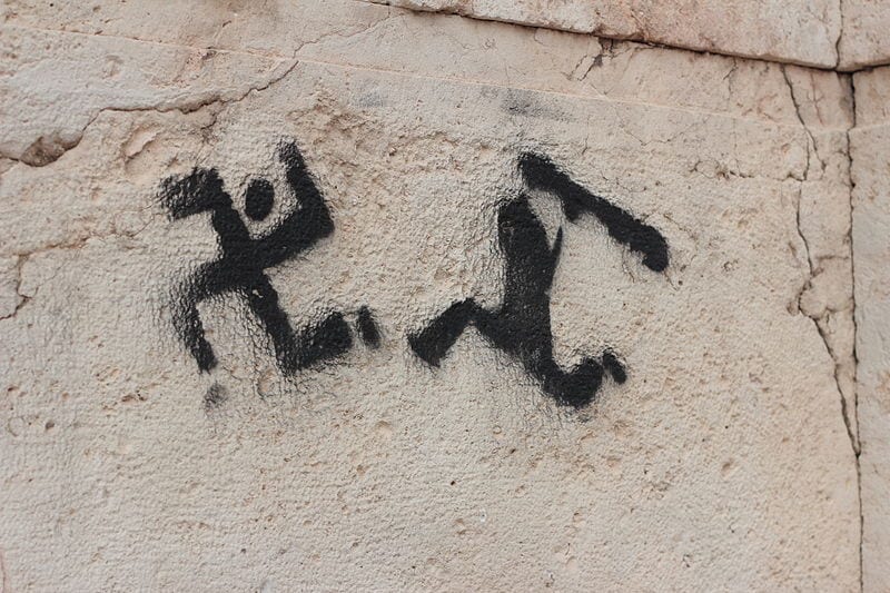 Political anti-nazism and anti-fascism propaganda graffiti in Athens, Greece photographed in 2013, showing a human figure trying to beat up a Nazi Party swastika resembling a running human.