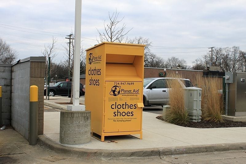 A Planet Aid clothing donation box sits on a curb in a parking lot.