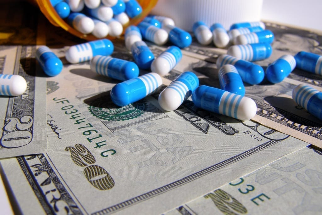 Blue and white capsules of an unknown prescription medication lay scattered atop twenty-dollar bills.