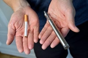Two hands offer a choice of a traditional cigarette or an electronic cigarette.
