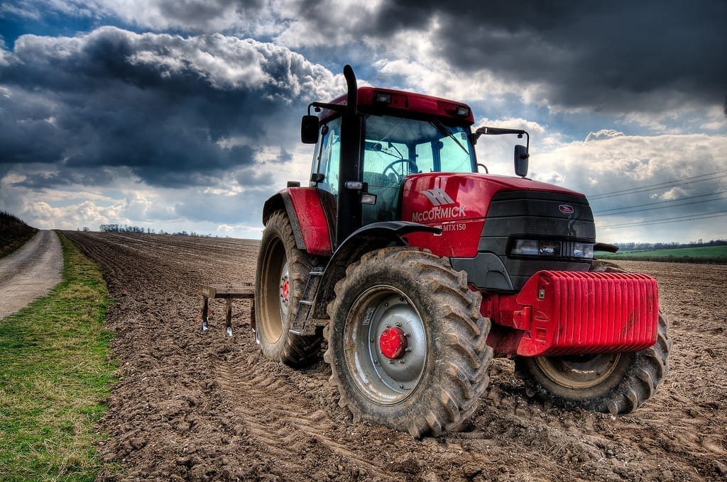 A driverless tractor sits parked in a plowed field, with ominous clouds in the background.