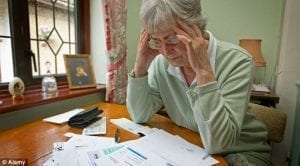 Older woman at table with bills; image courtesy www.dailymail.co.uk.