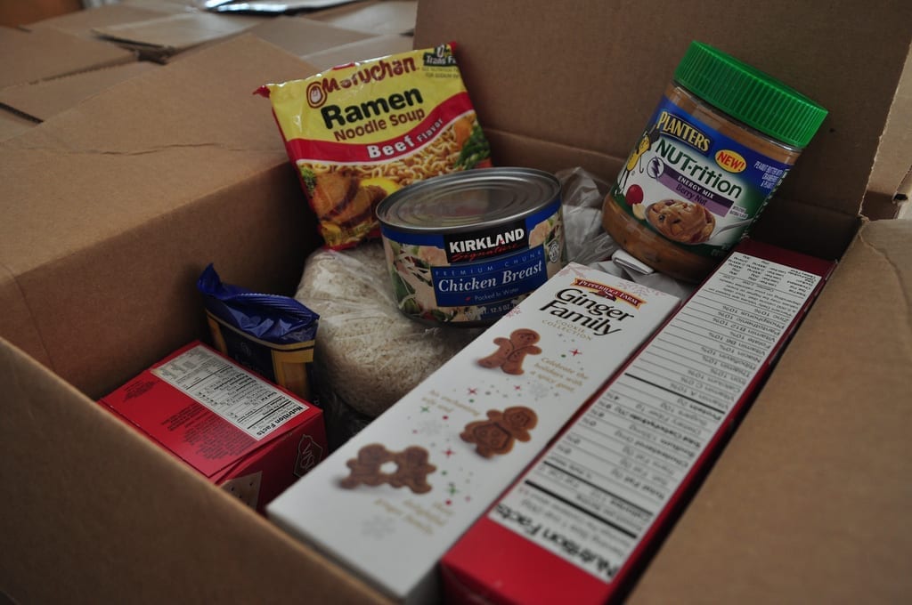 A box of donated, shelf stable foods like ramen, canned chicken, cookies, rice, and peanut butter, similar to what the harvest box might contain.