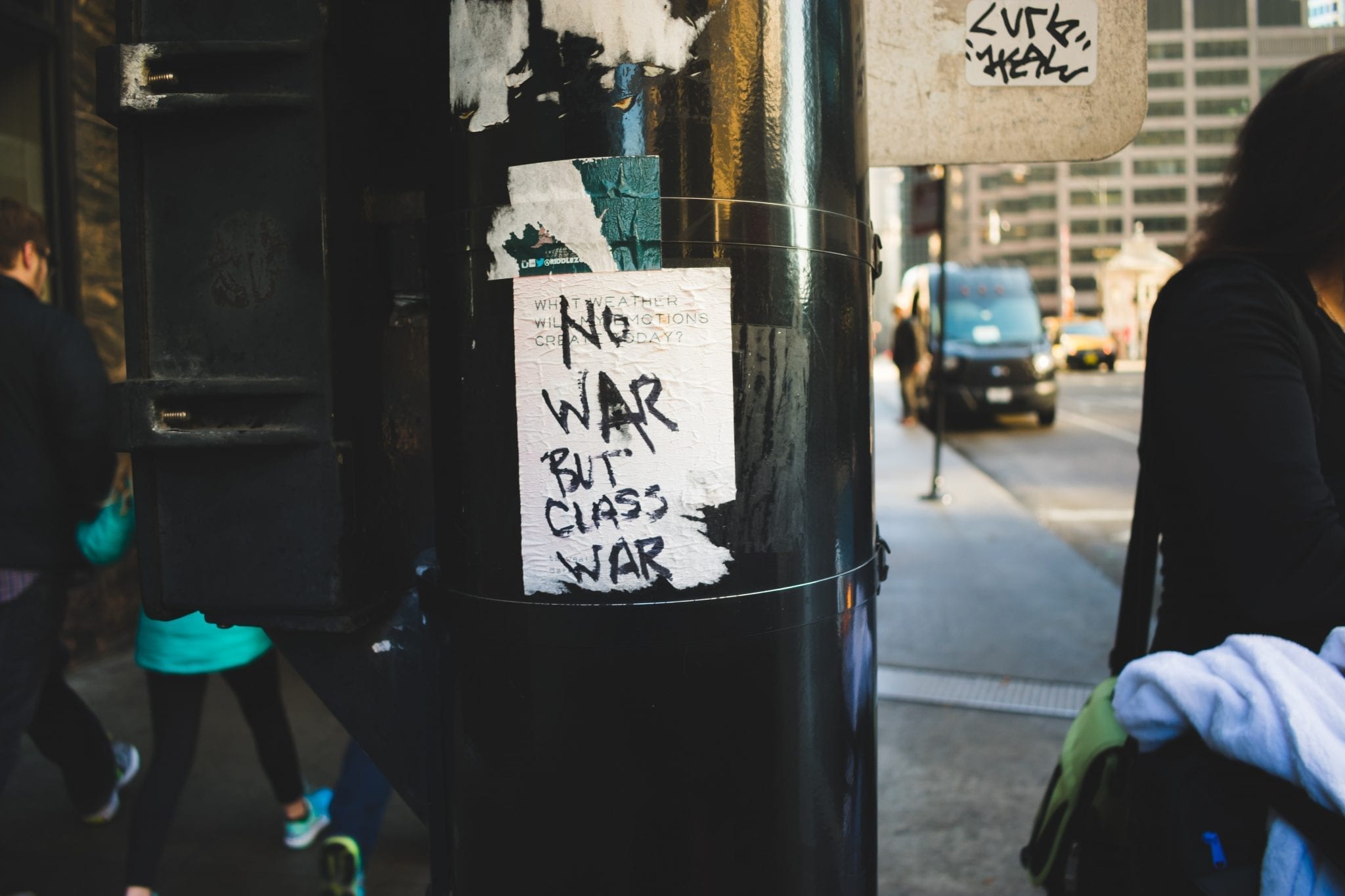 A handwritten sign on ripped paper attached to a pole in Chicago reads "No War But Class War."