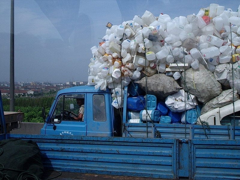 A blue pickup truck piled high with empty plastic jugs driven along a Chinese highway by a modern-day rag and bone man.