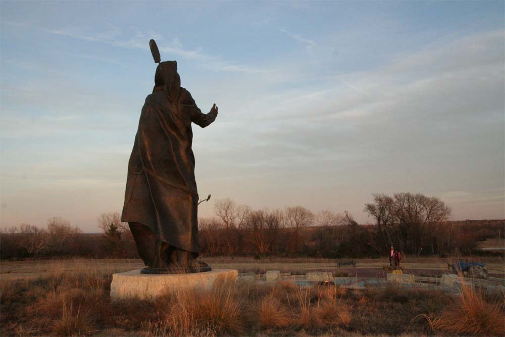 A larger than life statue of a Native American chief, from behind, at twilight.