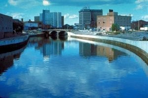 A calm river flows through an urban area, channeled between cement banks.