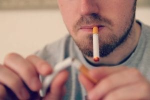 Man smoking e-cigarette while breaking a traditional cigarette in half; image by Vaping360.com, via Flickr, CC BY 2.0, no changes.