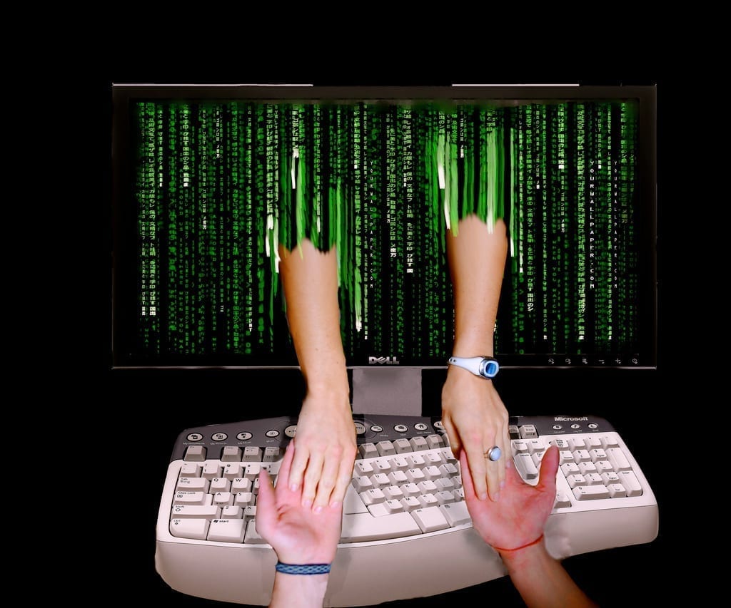 Online romance – man and woman joining hands through computer monitor; image by Don Hankins, via Flickr, CC BY 2.0, no changes.