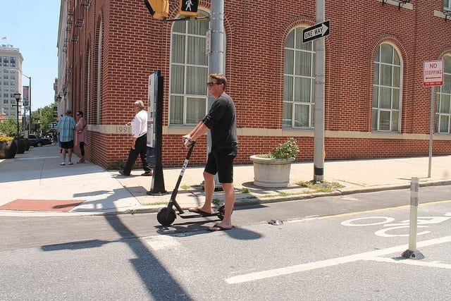 Man riding electric scooter; image by Elvert Barnes, via Flickr, CC BY-SA 2.0, no changes.