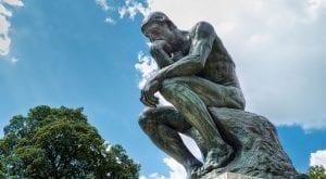 Rodin's classic statue of a man in thoughtful repose, photographed fro below, against a partly cloudy sky.