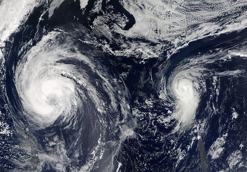 A satellite image of blue ocean and swirling cloud masses, including Hurricane Michael and a smaller Tropical Storm Leslie.