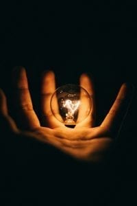 Hand with lightbulb floating above the palm against a dark background; image by Rohan Makhecha, via Unsplash.com.