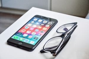 Smartphone displaying apps next to a pair of eyeglasses; image by David Švihovec, via Unsplash.com.