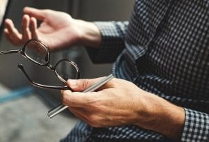 Person holding eyeglasses; image by Rawpixel, via Unsplash.com.