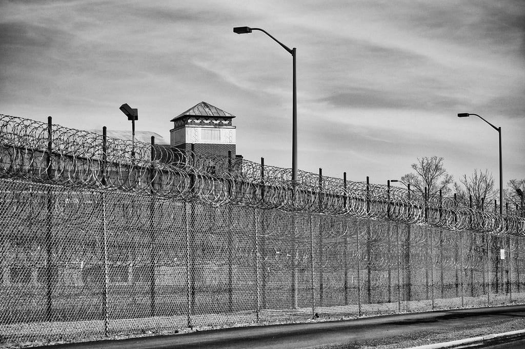 Black and white picture of a prison from outside the fence; image by Brad.K, via Flickr, CC BY 2.0, no changes.