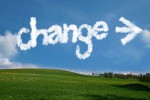 A green, grassy hill with a big blue sky. Among few clouds, the word CHANGE is written in white, puffy letters, with an arrow pointing to the right.