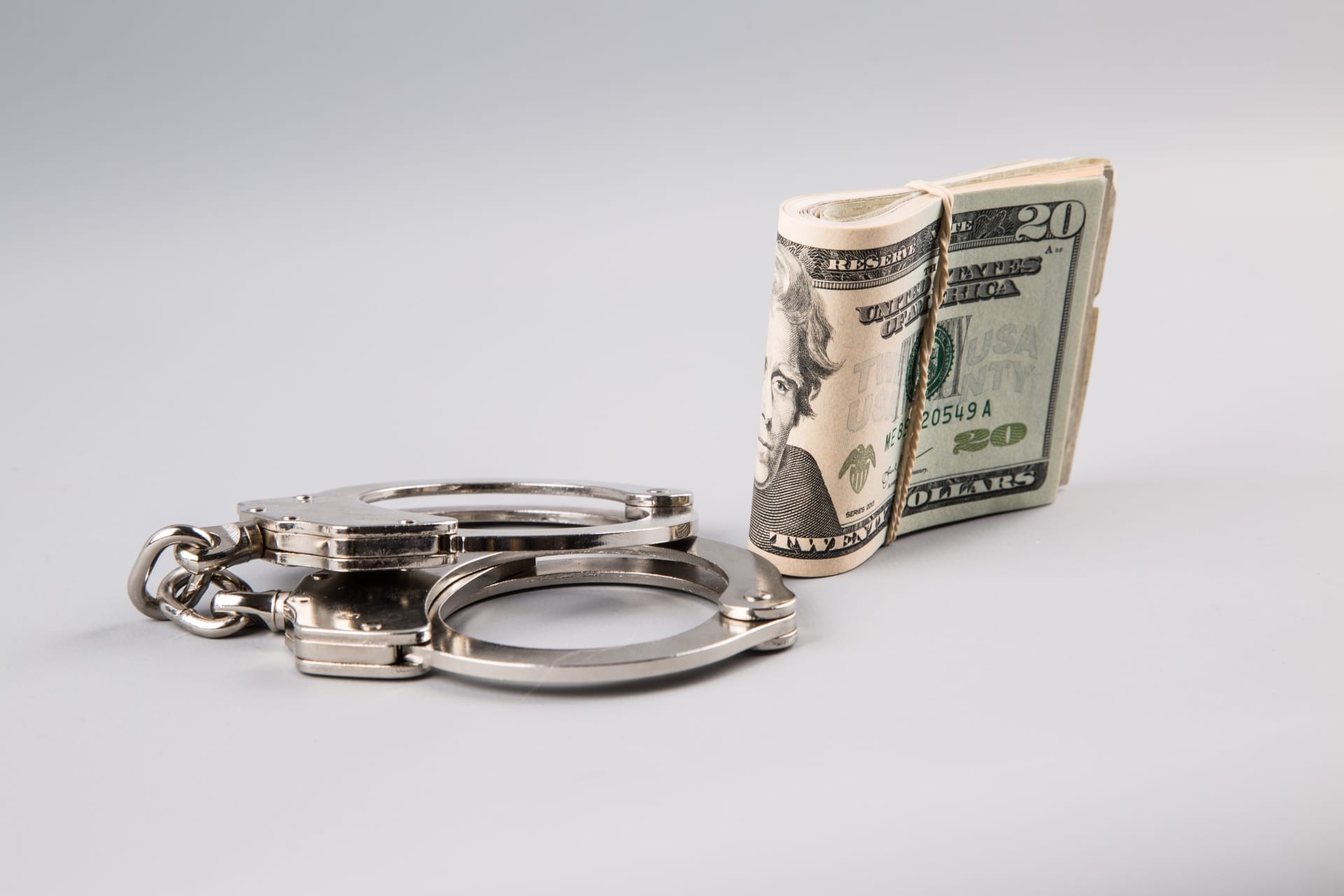 Handcuffs and money on grey background; image by George Hodan, via PublicDomainPictures.net, CC0.