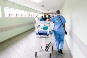 Woman wearing scrubs walking an incubator through hospital hallways. Image by Hush Naidoo, via Unsplash.com.