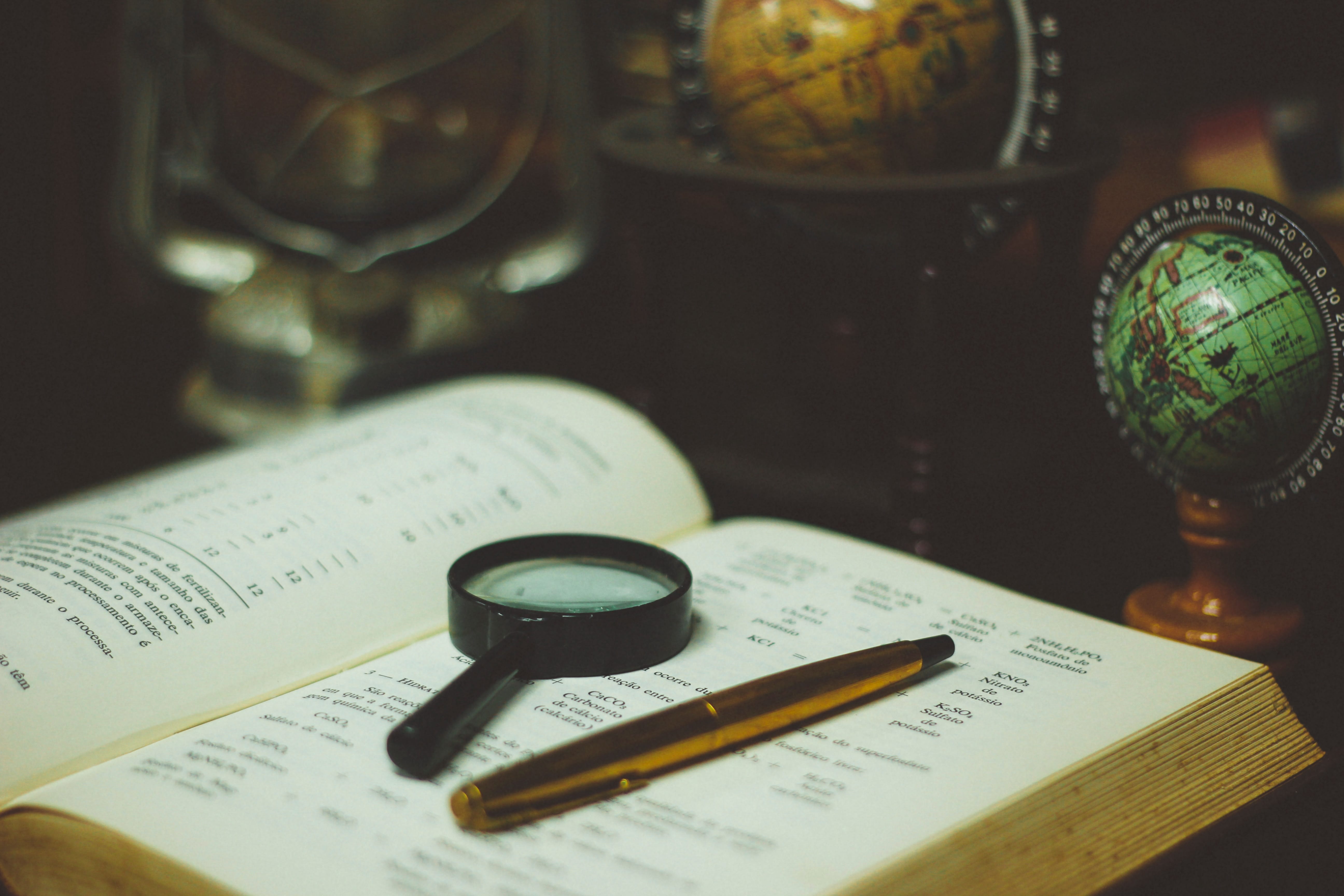 Magnifying glass and pen on book; image by João Silas, via Unsplash.com.