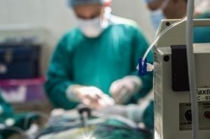 Out of focus shot of man in scrubs performing medical procedure; image by Marlon Lara, via Unsplash.com.