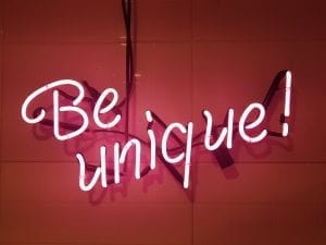 Pink neon sign on wall saying “Be Unique.” Image via PxHere.com, CC0.