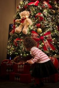 A curly haired toddler in a striped shirt explores the presents under a festively decorated Christmas tree.