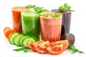 Four glasses of various fresh juices, surrounded by cut vegetables; image via PxHere.com, CC0.