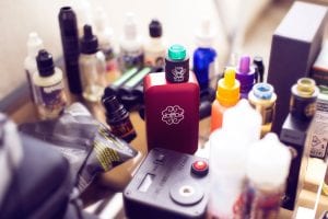 Red box mod vape beside e-juice bottles; image by Antonin FELS, via Unsplash.com.