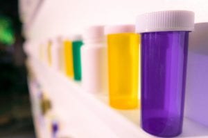 Empty prescription bottles on a shelf; image by Joshua Coleman, via Unsplash.com.