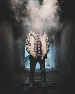 Young man in tunnel, face obscured by smoke; image by Luther Bottrill, via Unsplash.com.