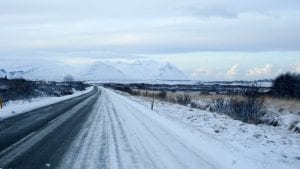 Snow-covered road flanked by fields with mountains in the distance; image by Patrick Wittke, via Unsplash.com.