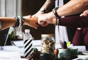 Fist bumps during team meeting; image by Rawpixel, via Unsplash.com.