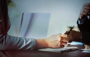 Person holding a pen at a meeting; image by Rawpixel, via Unsplash.com.