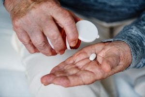 Man dispensing a white, oval-shaped pill from a bottle into his hand; image by Rawpixel, via Unsplash.com.