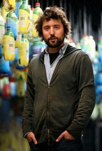 TerraCycle CEO and Loop partner Tom Szaky, hair askew, wearing a hoodie sweatshirt and standing in front of strings of plastic bottles.