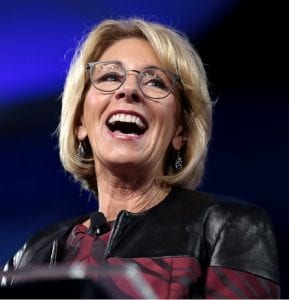 U.S. Secretary of Education Betsy DeVos, standing at a podium with a wide grin.