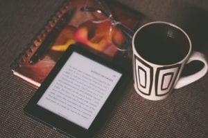 Black e-book reader beside white and black mug; image by Aliis Sinisalu, via Unsplash.com.