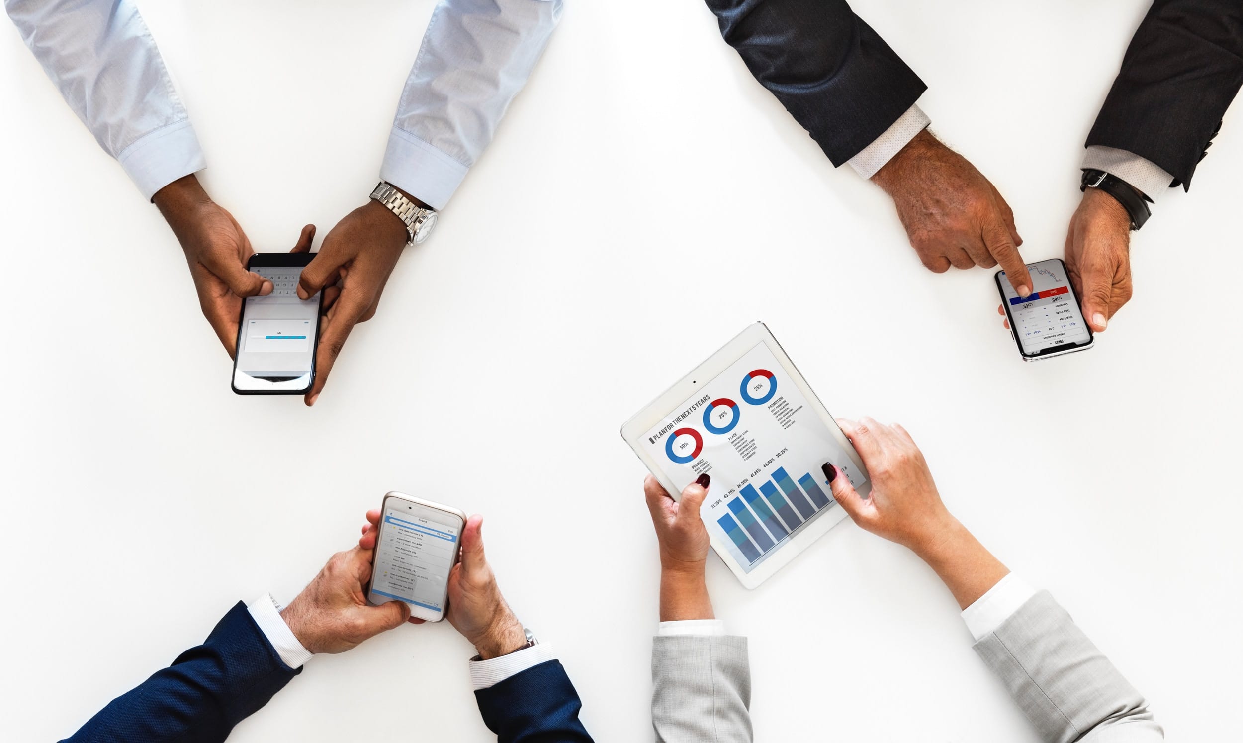 Four people using mobile devices at a meeting; image by Rawpixel, via Unsplash.com.