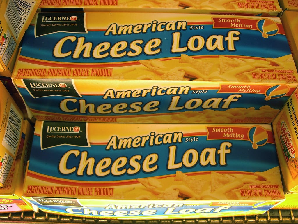 Stacked packages of Lucerne brand pasturized processed American cheese loaf food product.