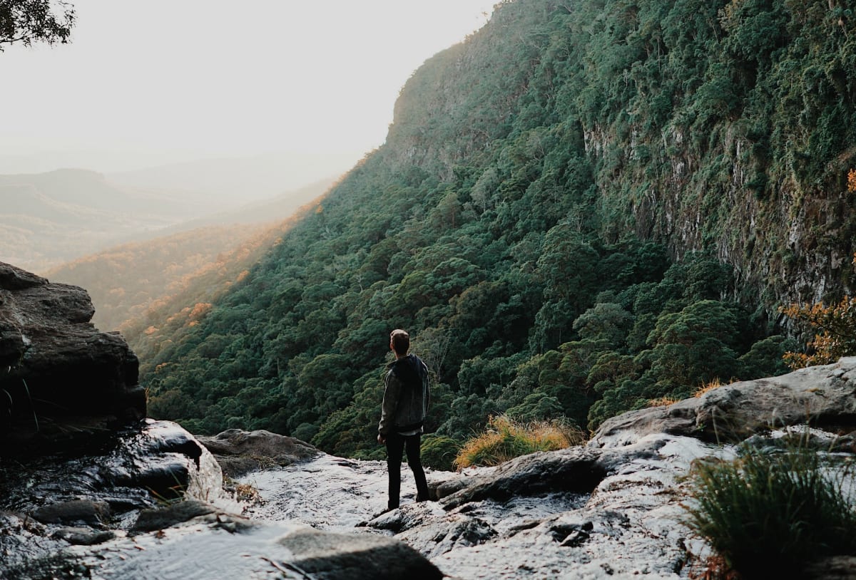 Man surrounded by hills and a stream looking at the horizon; image by Chris Fuller, via Unsplash.com.