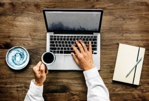 Man with laptop, cup of coffee, and journal; image by Rawpixel, via Unsplash.com.