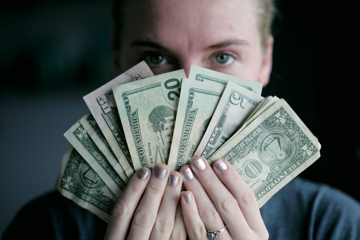 Woman holding money in front of her face; image by Sharon McCutcheon, via unsplash.com.
