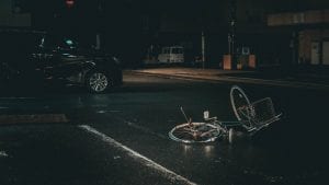 Bicycle in the middle of the street at night with black van nearby; image by Ian Valerio, via Unsplash.com.